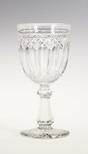  An intricate clear glass goblet with a pleated bowl, adorned with diamond and crisscross patterns, a leaf-like design below the rim, and a detailed stem, set against a light grey background. Artist name and title are unknown.