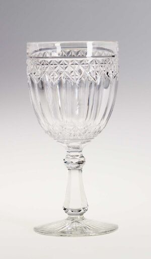 
 An intricately designed, clear glass goblet with decorative patterns on the bowl and a knobbed stem, set against a light grey background.