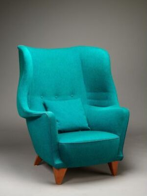  A plush turquoise upholstered armchair with wooden legs against a neutral gray background. The chair features a deep seat, padded armrests, and a high, tufted backrest with three buttons.