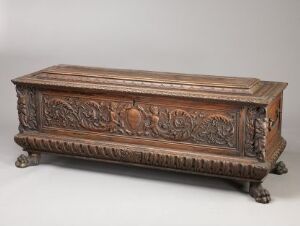  An antique wooden chest with intricate carvings and claw-and-ball feet on a neutral background, displaying a rich brown color palette and detailed artwork, suggesting Renaissance or Baroque style.