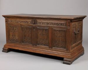  An antique dark brown wooden chest with ornate carvings on the front, placed against a neutral background, exemplifying traditional wood craftsmanship. Artistname: Unknown. Title: Unknown.