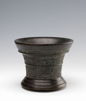  An antique dark gray metal vessel with decorative relief patterns encircling its exterior, featuring a slightly flared lip and a stable base, set against a light gray background.