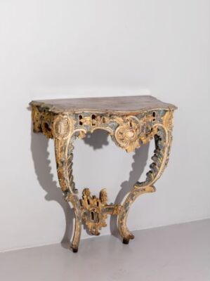  An ornate baroque-style table with a dark top and elaborate gold and cream carvings on its legs and body, set against a light grey background.