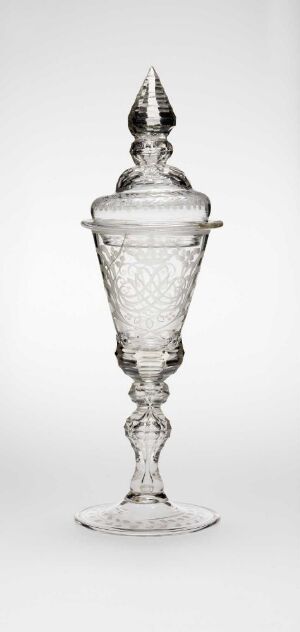  A finely crafted transparent glass covered goblet with intricate patterns and a pointed finial, set against a light background.