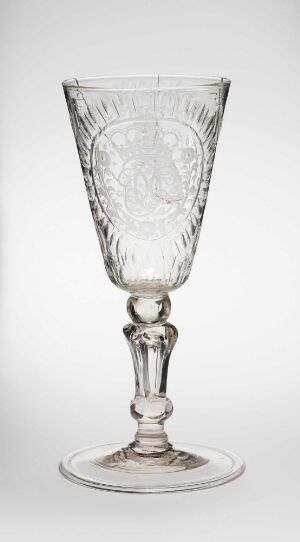  A clear glass goblet featuring a bell-shaped bowl with etched symmetrical patterns, an ornately shaped stem, and a broad, flat base, set against a light background.