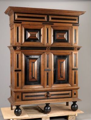  An intricate antique wooden cabinet with geometric paneling on the doors and ball-like feet, set against a neutral backdrop.