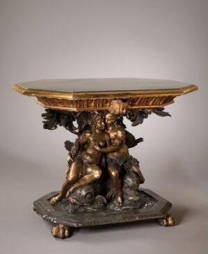  A gilded and carved wooden table by Heinrich Lorentzen Bech titled "Bord." The table has a decorative base featuring sculpted golden figures and a pine wood top with natural wood grain, detailed with gilded, carved edging.