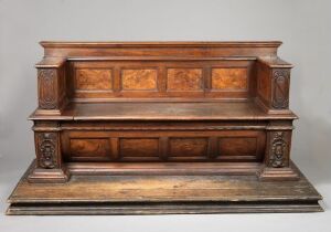  An antique wooden bench with intricately patterned back panels in a lighter brown set against a dark, deep brown frame, featuring a smooth seat, a panelled front that appears to have drawers, and decorative carved legs. The bench exudes a sense of traditional craftsmanship and sturdy design.