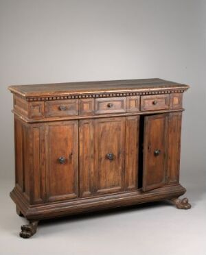  An antique wooden sideboard with decorative molding and carved details, featuring three drawers and two doors with metal handles and latches, supported by intricately designed legs ending in claw-like feet, set against a neutral background.