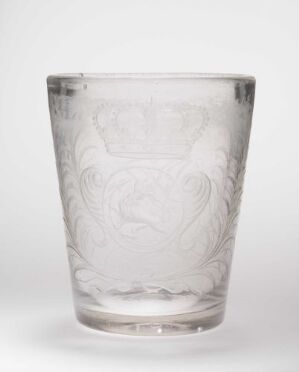  A clear glass cup with an etched floral design on a neutral background.