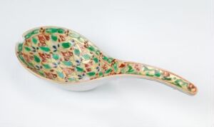  A porcelain spoon with the title "Bencharong" by an unknown artist, featuring intricate enamel color decorations in emerald green, red, and yellow floral patterns, set against a white background. The pattern is detailed, covering the spoon's surface with a stained-glass effect.