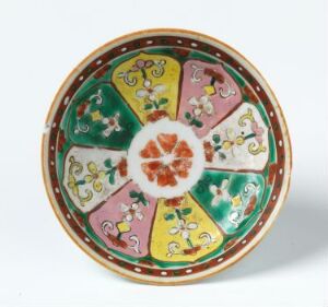  A wheel-thrown porcelain plate titled "Chan" by an unknown artist, with hand-painted enamel floral patterns in green and pink segments, a central orange-red flower motif, and a decorative rim with yellow and red concentric bands.