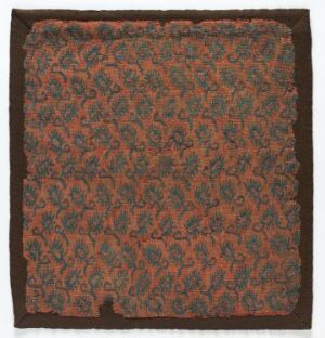  Intricately patterned textile with a dense floral motif in shades of orange, red, green, and teal on a dark brown background, suggesting a vintage or traditional fabric possibly used for decorative purposes.