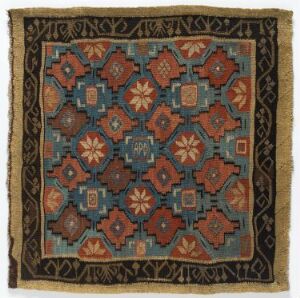  An intricately patterned square rug with a vibrant geometric design featuring star-like figures in turquoise, terracotta, beige, and navy blue, framed by borders with vine and leaf patterns in dark brown and beige on a slightly faded background, indicating probable historical value.