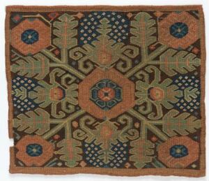  A square textile featuring a symmetrical pattern with a terracotta background and a central circular motif surrounded by stylized green, orange, and blue botanical elements, suggesting a traditional or historic design. Artist name and title are unknown.