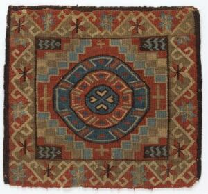  A square textile with an intricate, earthy-toned geometric pattern centered around a circular motif, surrounded by borders with stylized cross and arrowhead shapes, indicative of traditional craftsmanship.