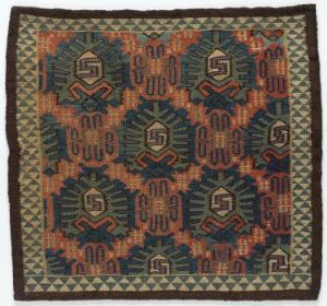  A square woven textile featuring a symmetrical pattern of stepped diamond shapes in rust, dark blue, and mint green on a brown background, surrounded by intricate geometric borders.