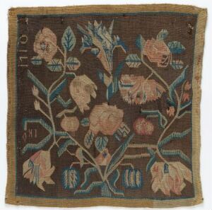  An antique square textile embroidered with pink and peach florals, varied green leaves, and small sections of white or light-colored text or numerical symbols, set against a mottled brown background. The piece exhibits a vintage, aged appearance with an arrangement that indicates skilled craftsmanship.