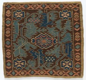  A square-shaped textile with a symmetrical pattern featuring a central medallion and corner quarter-medallions in shades of deep blue, red, cream, and golden-yellow, surrounded by a border with geometric and floral motifs, suggestive of Middle Eastern or Central Asian craftsmanship.