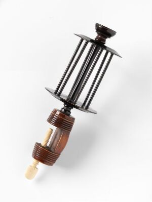  An antique syringe with a glass barrel encased in a cylindrical metal structure, topped with a dark plunger knob, and a ribbed conical section leading to a small, off-white needle tip, against a white background. Artistname and title remain unknown.