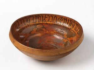  A shallow wooden bowl with a wide brim, featuring dark brown coloration at its center and a ring of decorative markings etched into its inner rim, set against an off-white background.