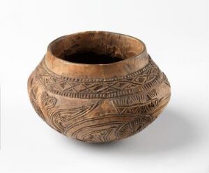  A pre-Columbian ceramic pot with detailed etched patterns in dark hues on a sandy tan background, exhibiting traditional geometric designs and sitting against a plain background with soft lighting.