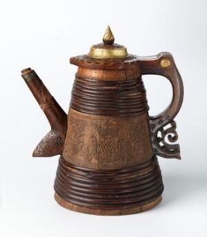  An ornate, possibly Middle Eastern or North African, dark brown metal coffee pot with horizontal grooves, embossed patterns, an intricately designed handle, and a golden finial on the lid, displayed against a white background.