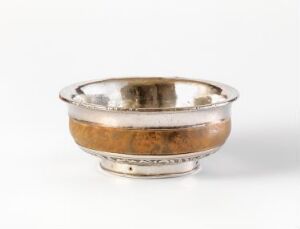  A shallow, silver-colored bowl with a curled rim and decorative foot, reflecting warm and cool tones, set against a white background.