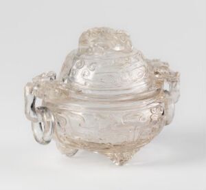  An ornately crafted glass container with a lid and scroll-like handles, featuring intricate embossed designs and a frosty translucent appearance, showcased against a neutral background. Artist name and title are unknown.