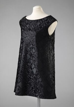  A sleeveless black dress with a textured pattern displayed on a mannequin against a light gray background, reflecting a classic and elegant design. Artistname and title unknown.