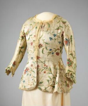  A vintage ivory jacket with a detailed floral pattern in red, blue, green, yellow, and pink on a mannequin against a grey background. The jacket has long sleeves with flared cuffs and a slightly flared waist with no visible closures.