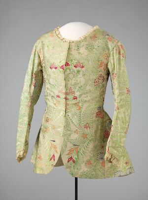  A historic pale green floral-patterned woman's bodice with delicate red and pink flowers, displayed on a mannequin against a neutral gray background. The garment features slim sleeves, structured shoulders, and decorative front closures. The condition suggests careful preservation of this piece of period clothing.