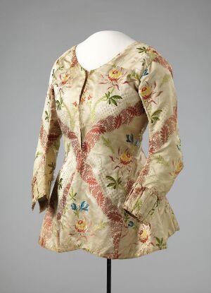  A historical beige bodice with a multicolored floral pattern, displayed on a headless white mannequin against a grey background.