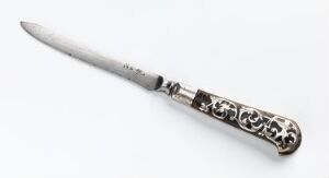  An intricately designed knife with an ornate handle and a silver-gray blade, set against a neutral off-white background.