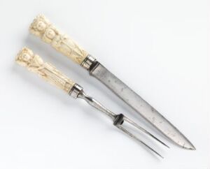  An antique ivory-handled knife and fork with intricate carvings and etched metal designs, set against a plain white background.