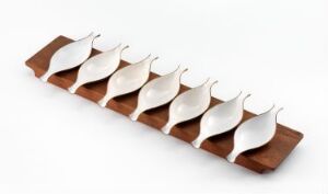  "Sildebordet" by J. Tostrup, a decorative teak serving board featuring eight silver fish-shaped figures aligned in a row against the rich, warm brown grain of the wood.