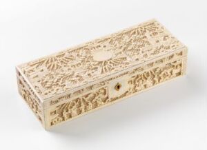  An intricately carved, light-colored rectangular box, possibly made of ivory or pale wood, with detailed floral and foliage designs and a small lock on one end, set against a neutral off-white backdrop.