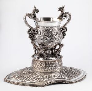  The "Sølvbolle" by Henrik B. Møller, a silver bowl on a decorative tray with chased patterns and sculptural handle figures, displaying exquisite craftsmanship.