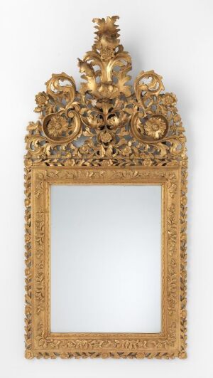 An elaborate and decorative vertical golden mirror frame with detailed gild work and an ornate crest at the top.