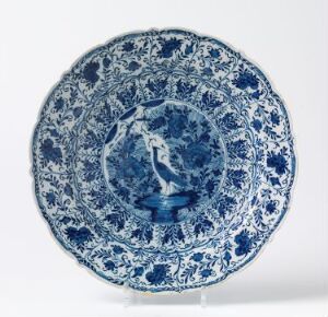  A decorative ceramic plate featuring a blue and white design with intricate patterns and a central pastoral motif.