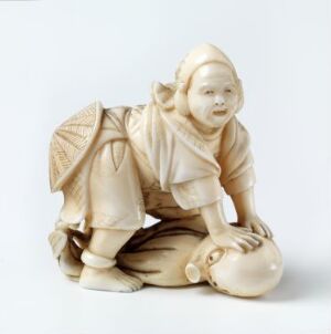  Sculpted figurine of a child in traditional attire crouching and playing with a ball, crafted in varying shades of cream and light beige, set against a plain white background.