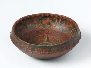  An ornate, seemingly antique terracotta-colored bowl with decorative patterns including a central medallion, concentric circles, and a text band on the exterior viewed on a plain, neutral background.