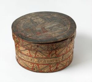  Antique round box with fitted lid, decorated with geometric and organic motifs in earthy tones of red, beige, brown, and muted green, showing signs of age and historical craftsmanship.