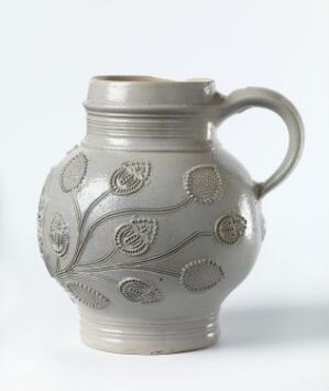  A silver-gray pewter jug with embossed floral patterns and beaded motifs on a white background.