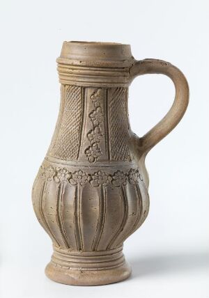  A traditional ceramic pitcher with a flared neck, detailed with embossed floral designs, and a single handle, in a sandy beige color.