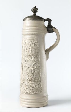  An off-white traditional ceramic beer stein with metal lid and handle, featuring intricate embossed designs, on a plain white background.