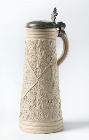  An intricately carved traditional beer stein with a hinged pewter lid and thumb lever, featuring detailed scrollwork and floral bas-relief designs, set against a plain light background.