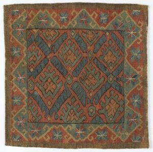  An image of a square-shaped traditional textile with intricate geometrical and abstract patterns in earthy tones of rusty red, green, teal, mustard yellow, and white, featuring a central diamond-like lattice surrounded by a stylized foliage border.