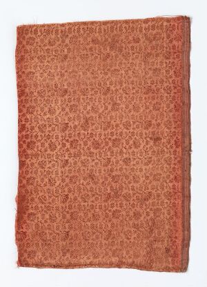  A textured fabric or canvas with a dense pattern of circular motifs in a warm, rusty terracotta color, displaying an organic and handcrafted quality.