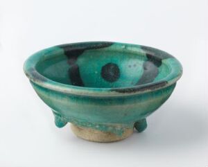  A small, flared ceramic bowl with a lustrous emerald green glaze and mottled effects standing on a simple foot, displaying the bowl's artisanal character.